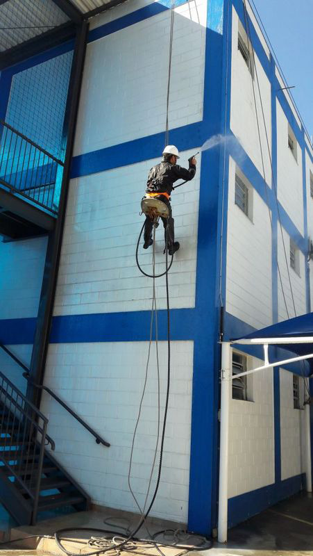 Hidrojateamento em fachada, trabalhador equipado com capacete em cadeira suspensa, rapel, fazendo a limpeza de fachada de prédio com hidrojateamento.